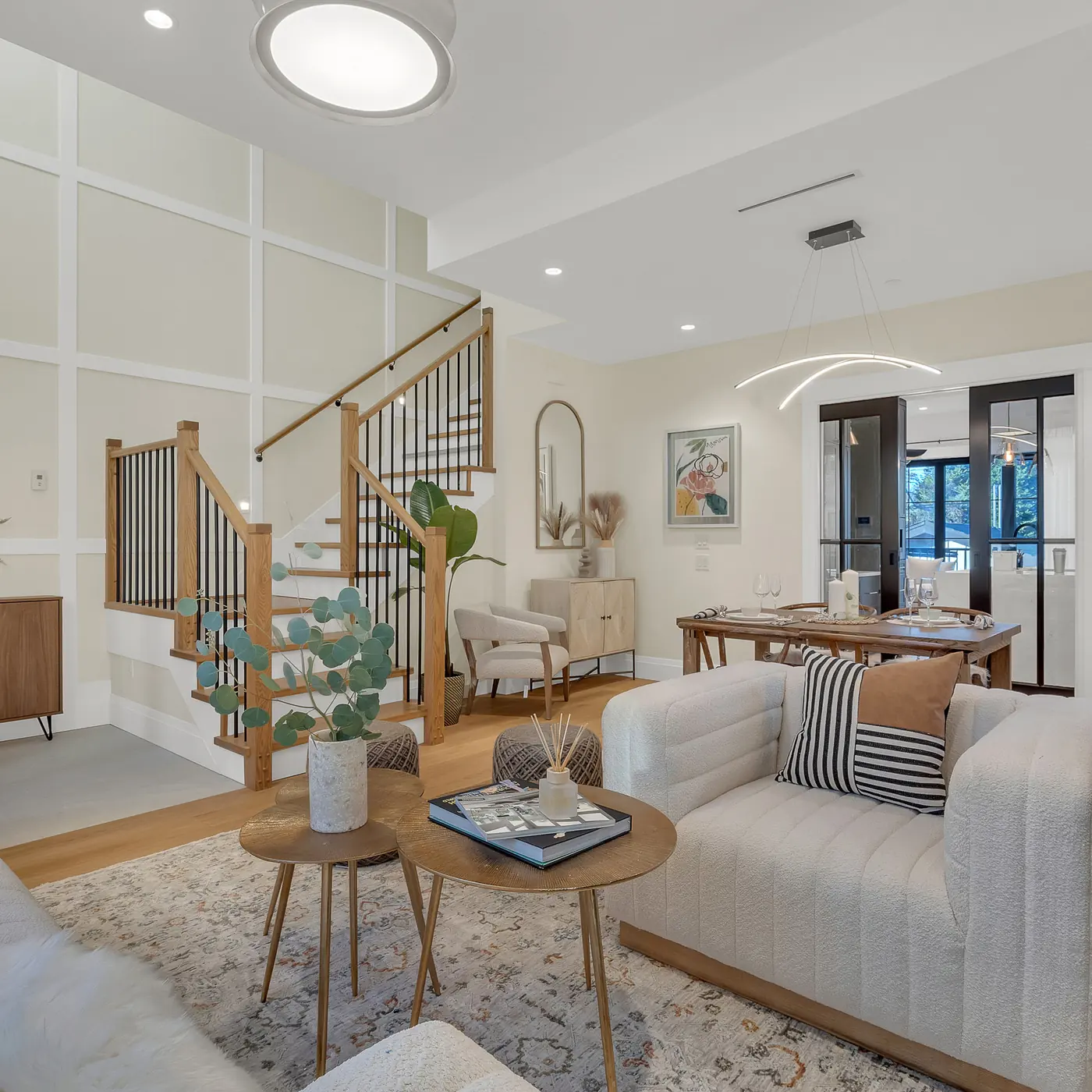 Living room with a wood stair railing, black metal balusters, white panelled walls and an open dining area