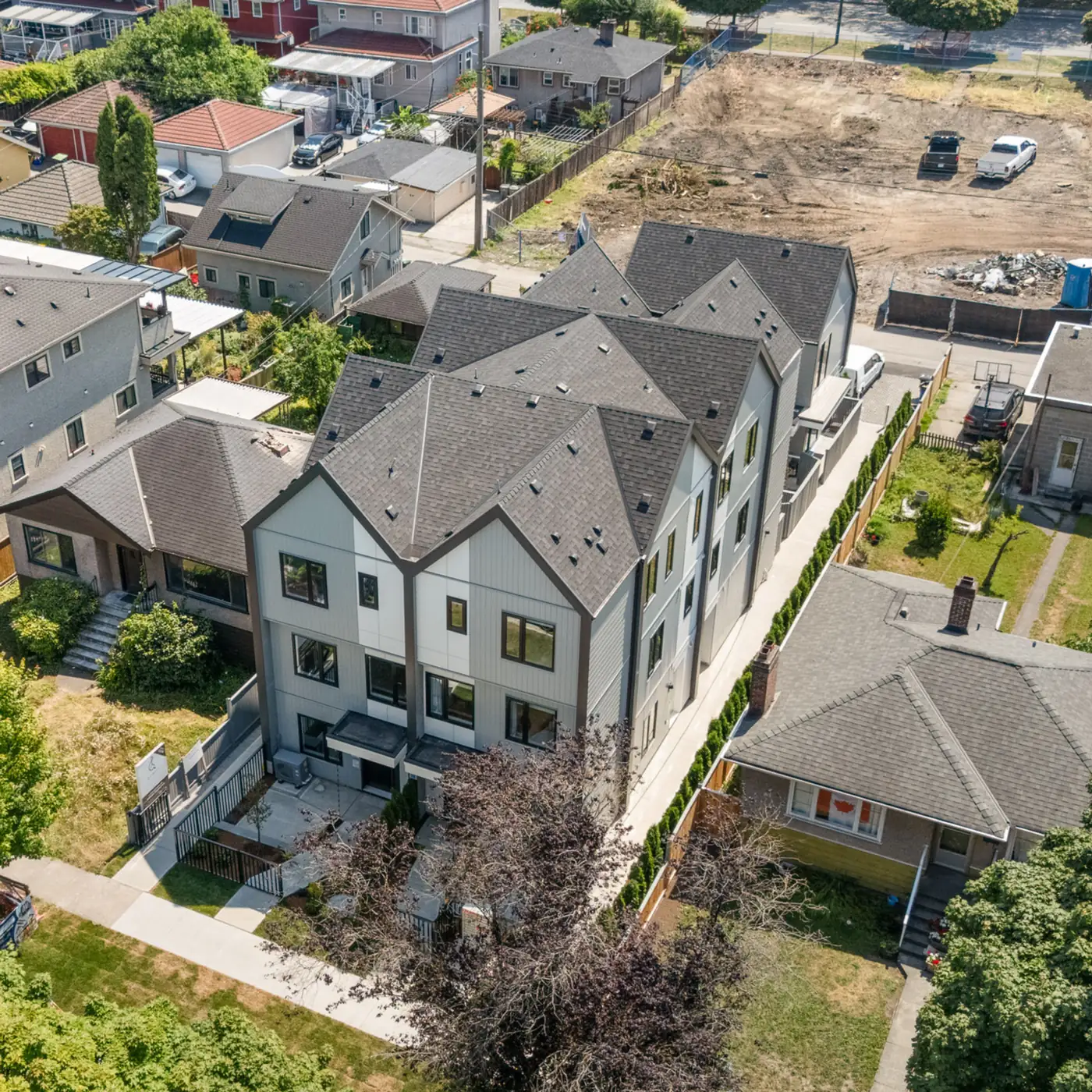 Aerial view of a row of gabled townhomes beside a cleared lot