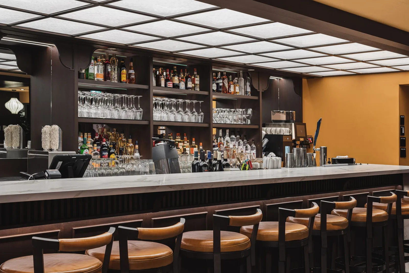 Bar counter and stools in front of glass and bottle shelves, Linh Noodle Bar by Costar Construction, Vancouver