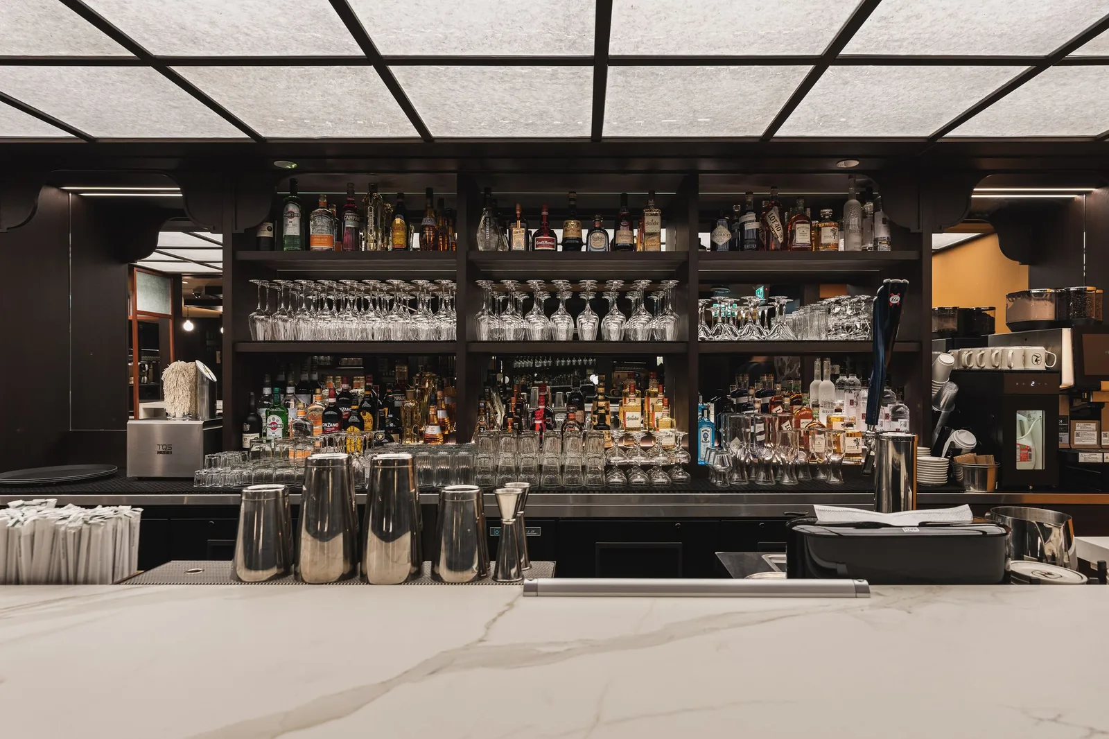 Back bar with glass racks and bottle shelves below the lit ceiling, Linh Noodle Bar by Costar Construction, Vancouver